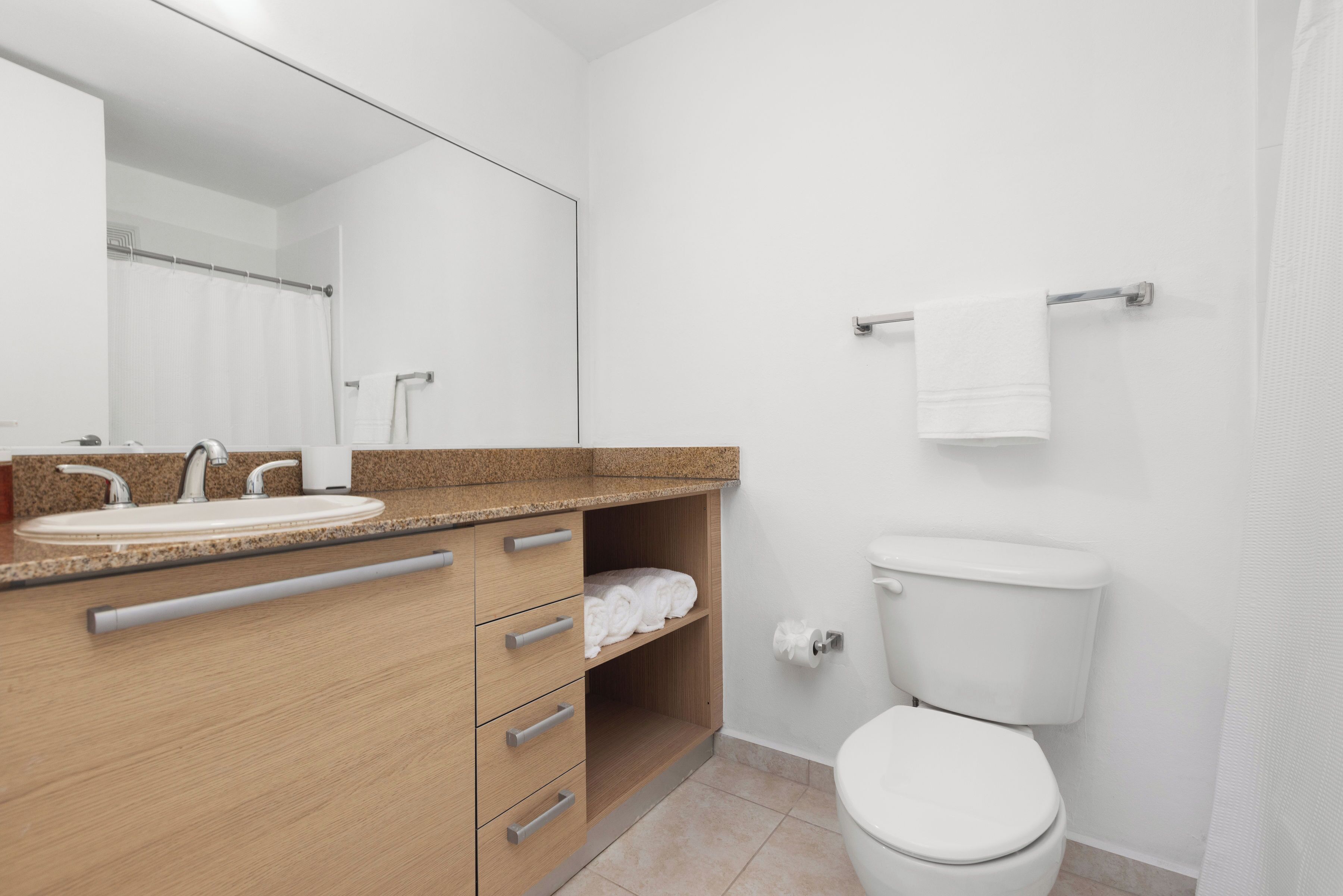 Un baño moderno con tocador de madera, lavamanos, inodoro y un espejo grande.
