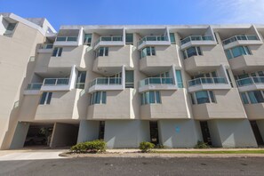 Un edificio residencial de varios pisos con balcones, garaje para coches y jardineras.