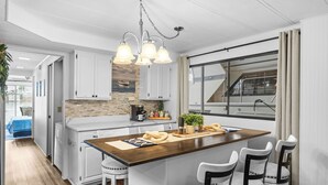 Une cuisine moderne avec des meubles blancs, un îlot central en bois et une vue sur un bateau, visible à travers une grande fenêtre.