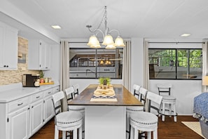 A modern kitchen with white cabinets, a wooden dining table, and pendant lighting.