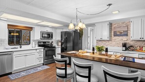 Une cuisine moderne avec des meubles blancs, un îlot central doté de tabourets, des appareils en acier inoxydable et un luminaire suspendu.