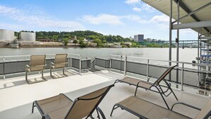 Une terrasse de bateau avec des sièges et une vue sur une rivière et un pont.