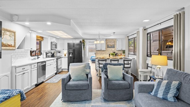 Une cuisine moderne avec des meubles blancs, un coin repas comprenant une table et des chaises, et un salon avec un canapé et des fauteuils.