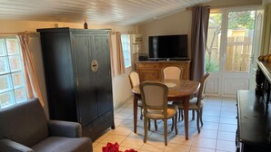 Uma sala de jantar com mesa e cadeiras de madeira, um armário escuro, uma televisão e um vaso com flores vermelhas.