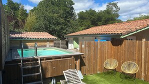 Quintal com piscina, deck de madeira e duas cadeiras de vime.