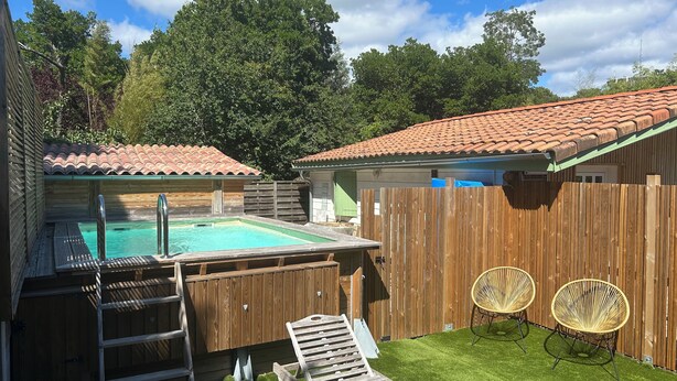 A backyard with a swimming pool, wooden deck, and two wicker chairs. - 🌿 Le Cabanon de Cassy - Comfortable gîte with heated pool, near the ocean (Lanton)