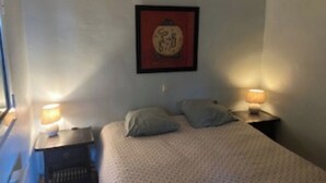 Quarto pequeno e bem organizado, com uma cama de solteiro, duas luminárias de cabeceira e um quadro na parede.