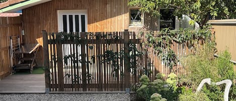 A wooden house with a gravel driveway, a wooden fence, and various plants.