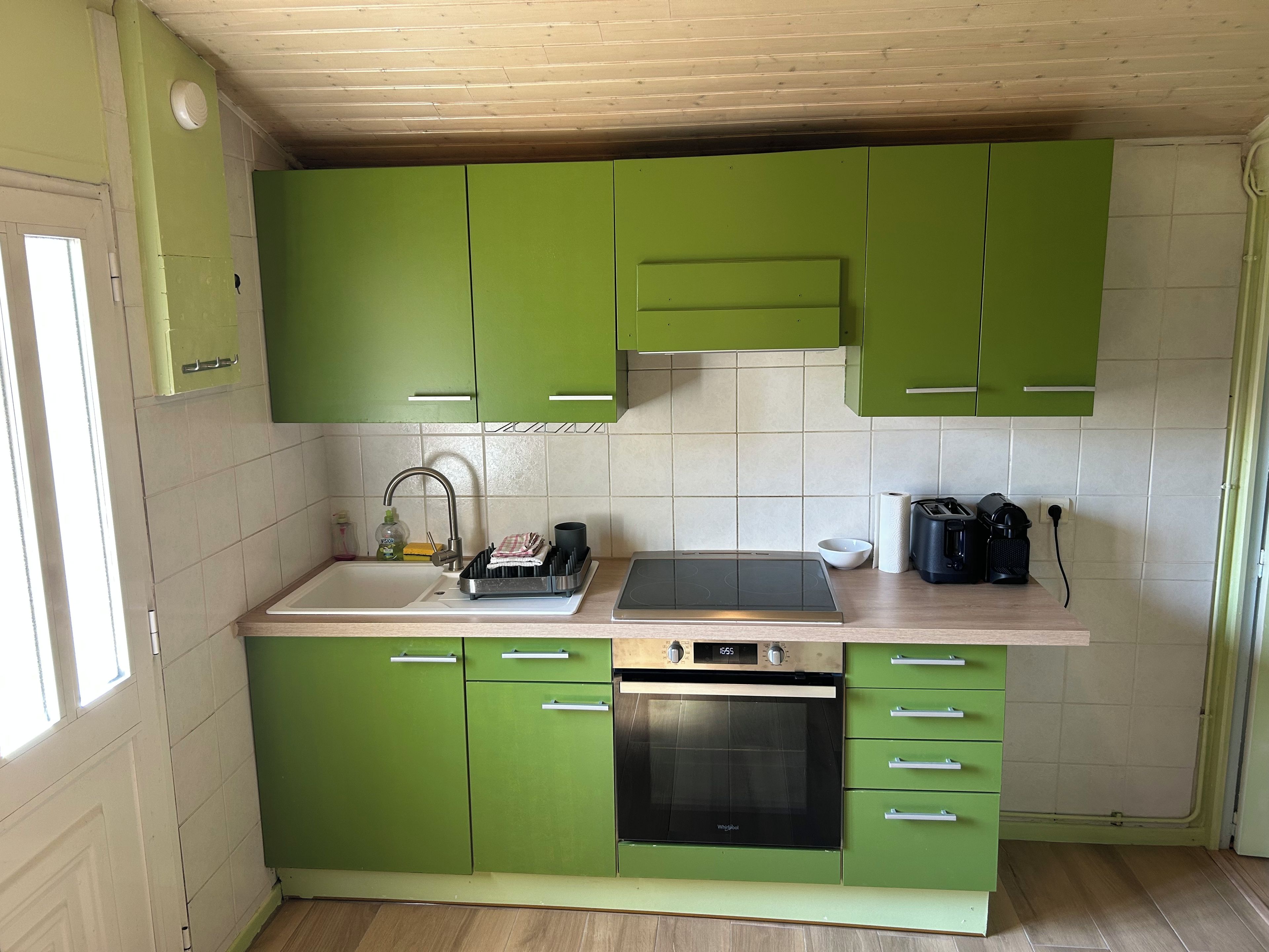 A kitchen with green cabinets, a stainless steel sink, a built-in oven, and a countertop with a kettle and a toaster.