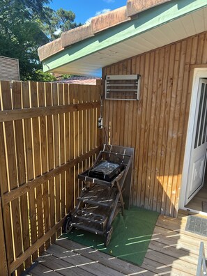A wooden deck with a grill, a green artificial turf, and a wooden fence.