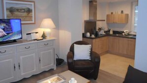 A modern living room with a flat-screen TV, a white cabinet, a brown leather chair, and a small table with a tray.