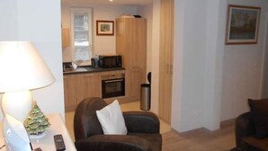 A compact living space with a kitchenette, a dining area with a table and chairs, and a small decorative tree on a side table.