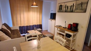 Un espai habitable compacte amb zona de menjador, sofà, televisió i cafetera.