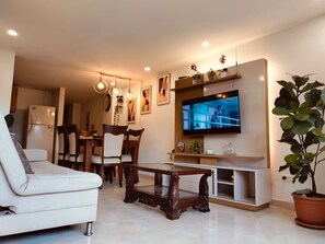 Ein Wohnzimmer mit Sofa, Couchtisch, Fernseher, Essbereich und einer Zimmerpflanze.