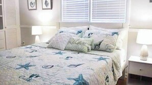 A bedroom with a bed, two bedside tables, a window with blinds, and wall-mounted artwork. - Private Home Game Room Backyard (Centerville)
