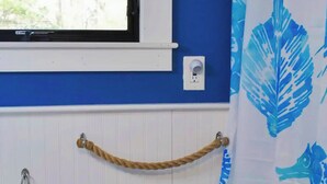 A bathroom with a blue wall, a white window, a white electrical outlet, a white towel rack with a rope, and a blue and white shower curtain. - Private Home Game Room Backyard (Centerville)