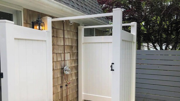 A white wooden outdoor shower enclosure with a metal faucet and a lantern on the wall. - Private Home Game Room Backyard (Centerville)