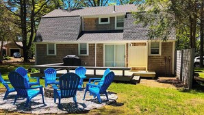A two-story house with a patio area featuring blue Adirondack chairs and a grill. - Private Home Game Room Backyard (Centerville)