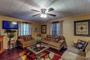 Ein Wohnzimmer mit Deckenventilator, zwei Sofas, einem Couchtisch und einem Flachbildfernseher.