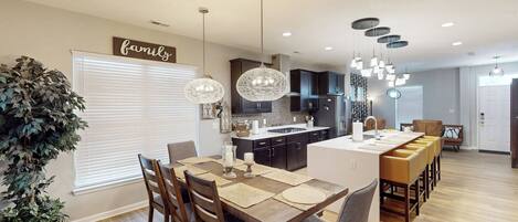Une cuisine moderne avec des meubles de couleur sombre, un îlot central et des luminaires suspendus.
