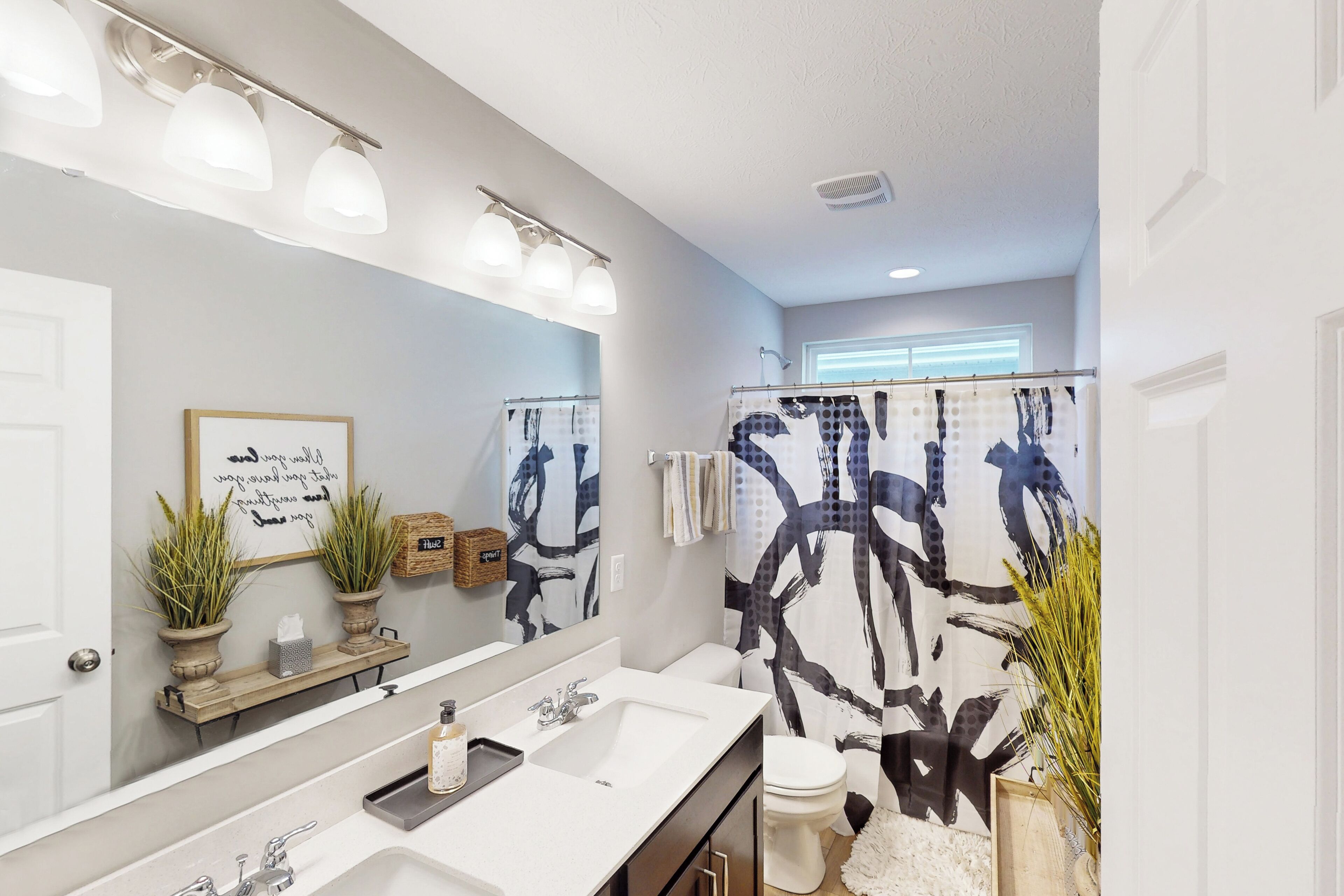 A bathroom with a large mirror, two sinks, a toilet, and a shower with a black and white abstract shower curtain.