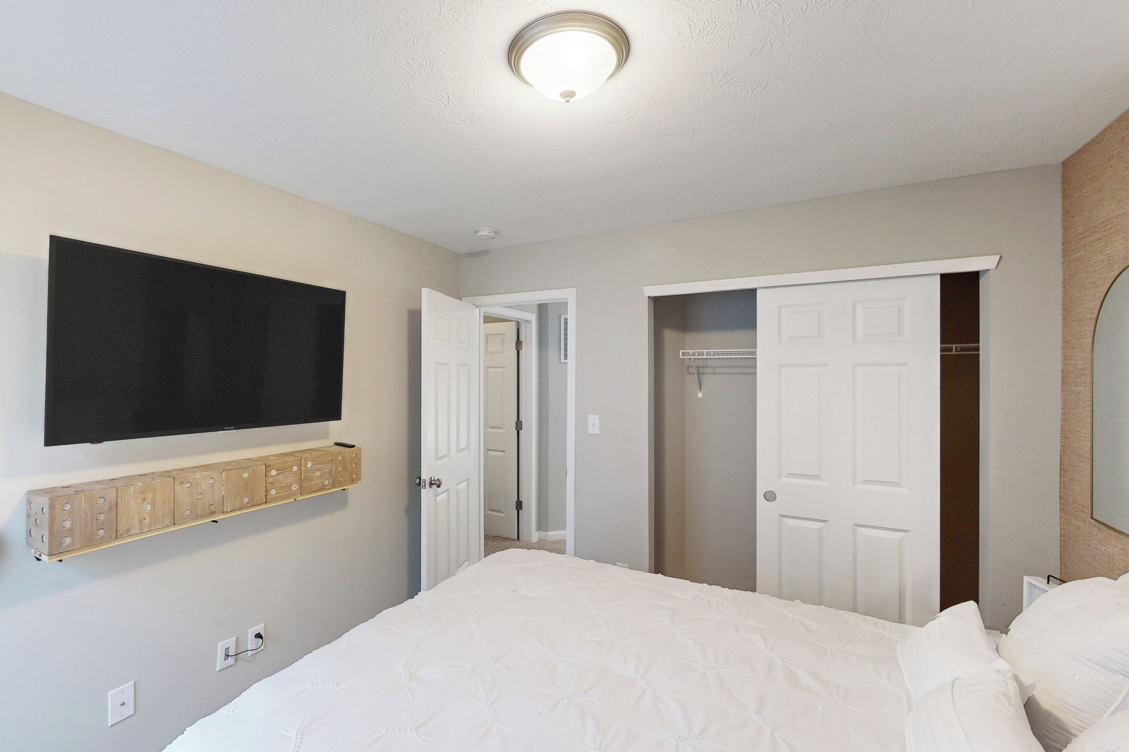A bedroom with a bed, a mounted TV, a wooden storage unit, and a closet.