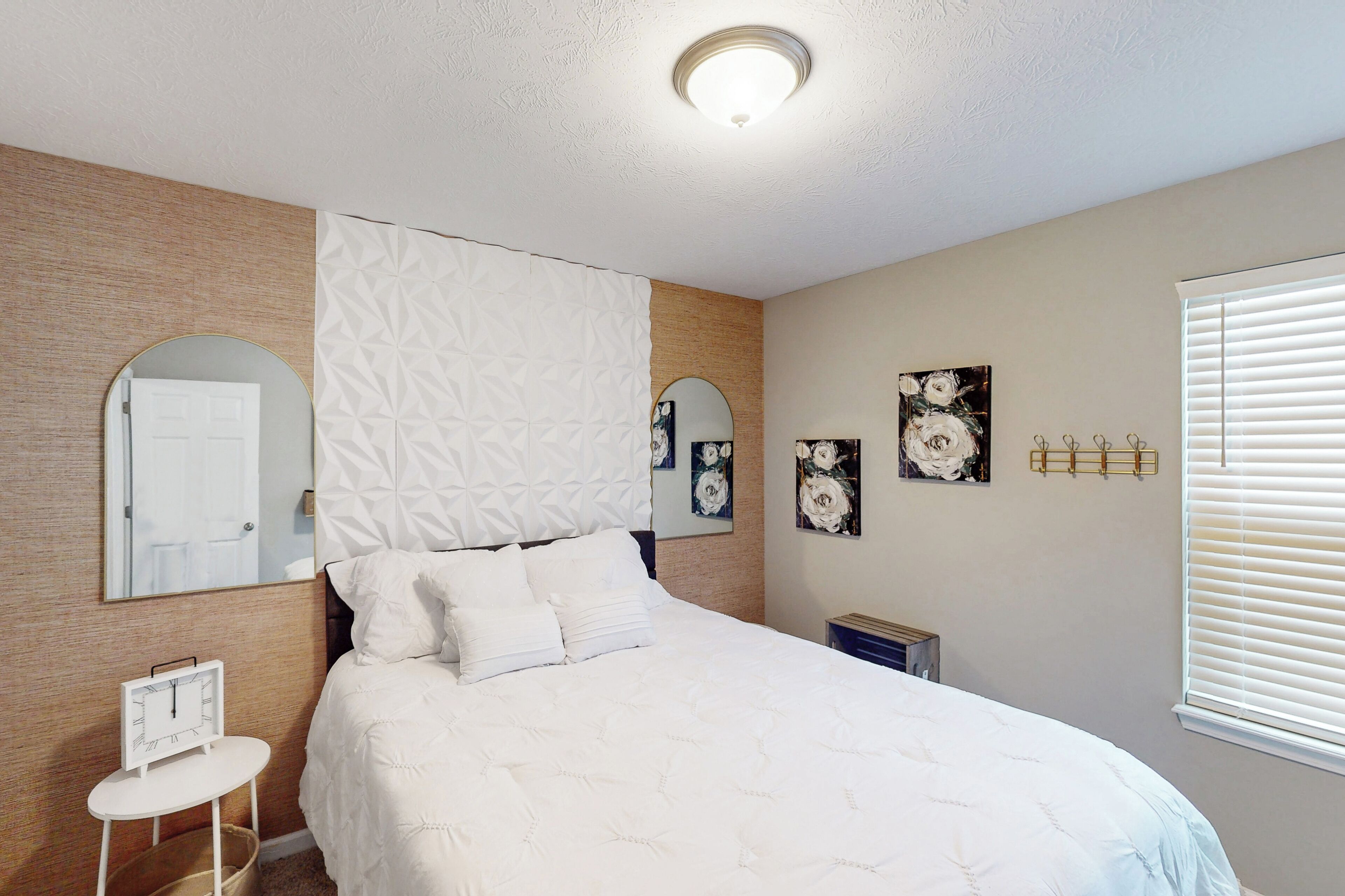 Quarto com cama, espelho redondo, relógio e janela com persianas.