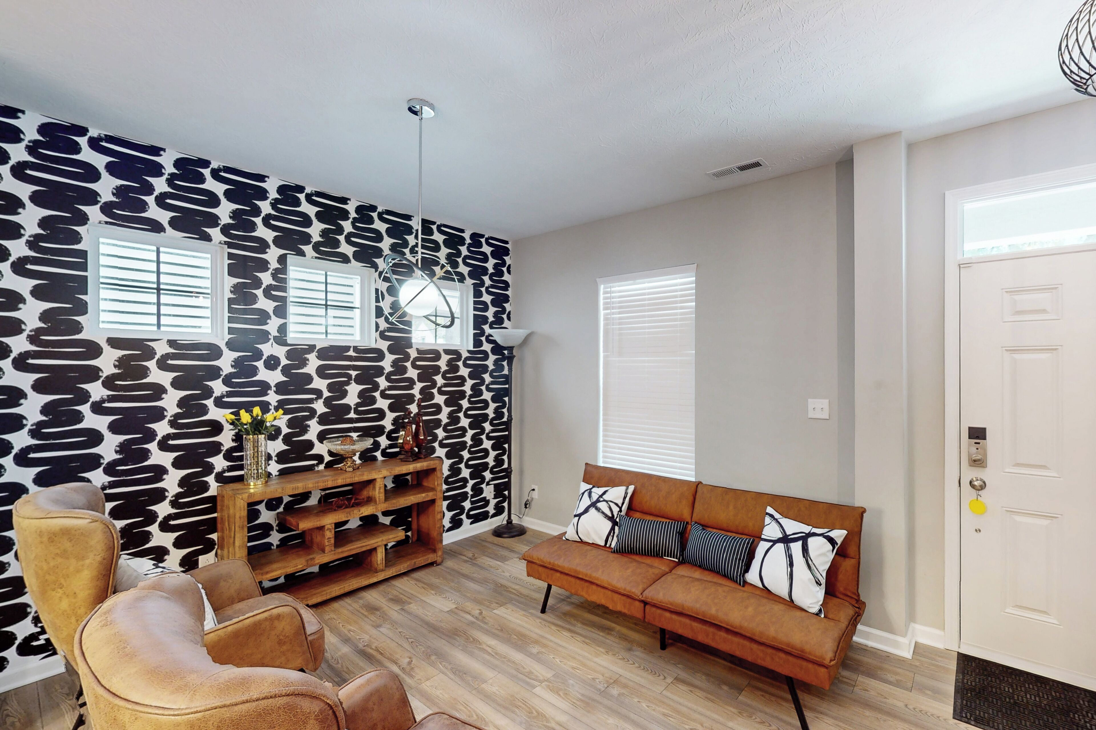 Una sala de estar con una pared de diseño de piedra, piso de madera, un sofá de cuero marrón, una mesa de centro de madera y una mesita auxiliar con objetos decorativos.