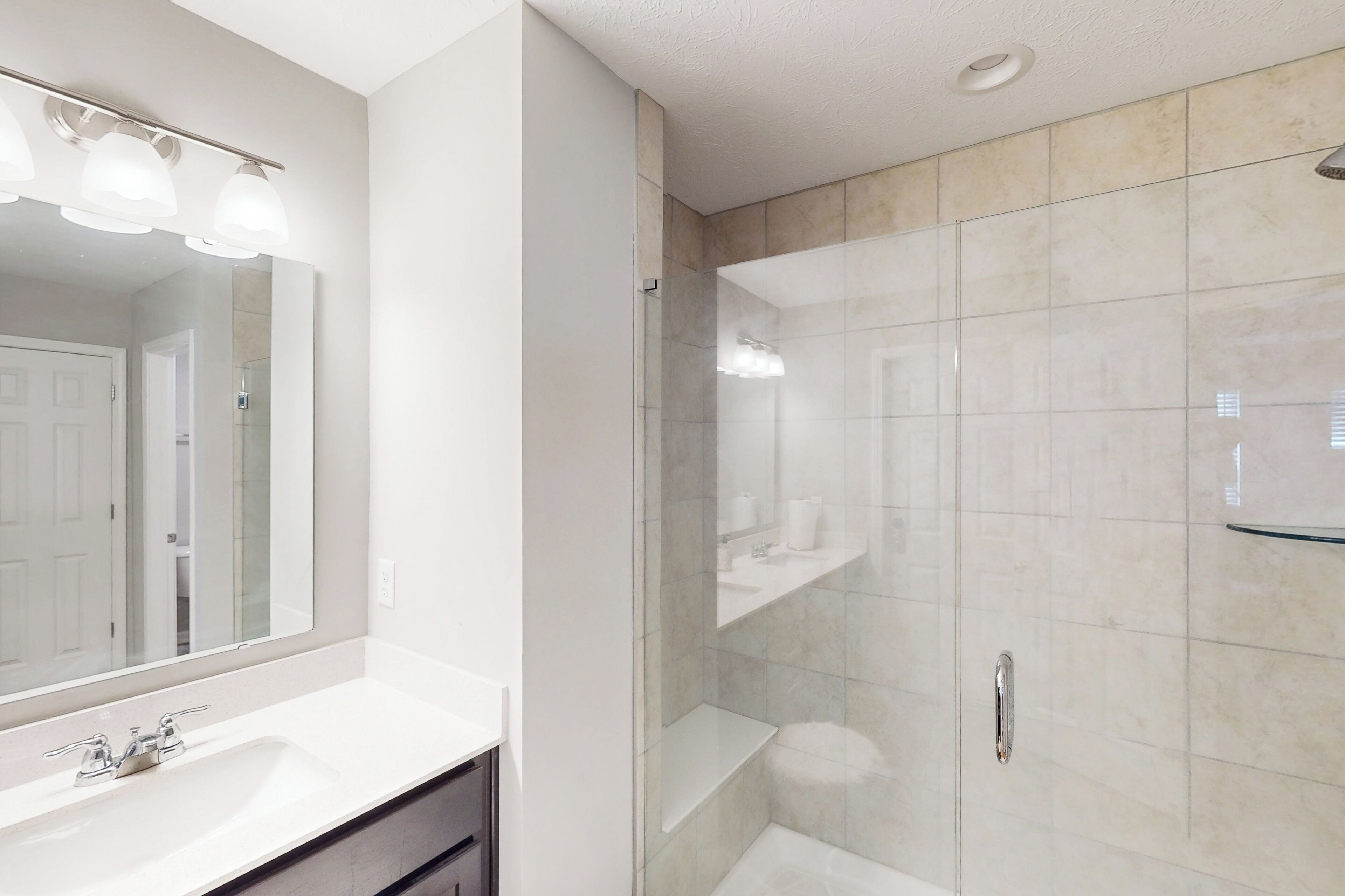 A modern bathroom with a large mirror, a white sink, and a glass-enclosed shower area.