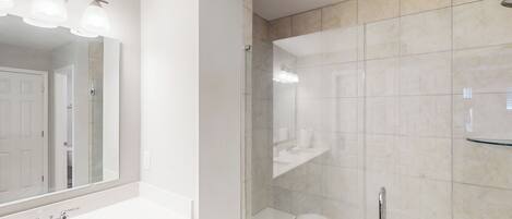 A modern bathroom with a large mirror, a white sink, and a glass-enclosed shower area.
