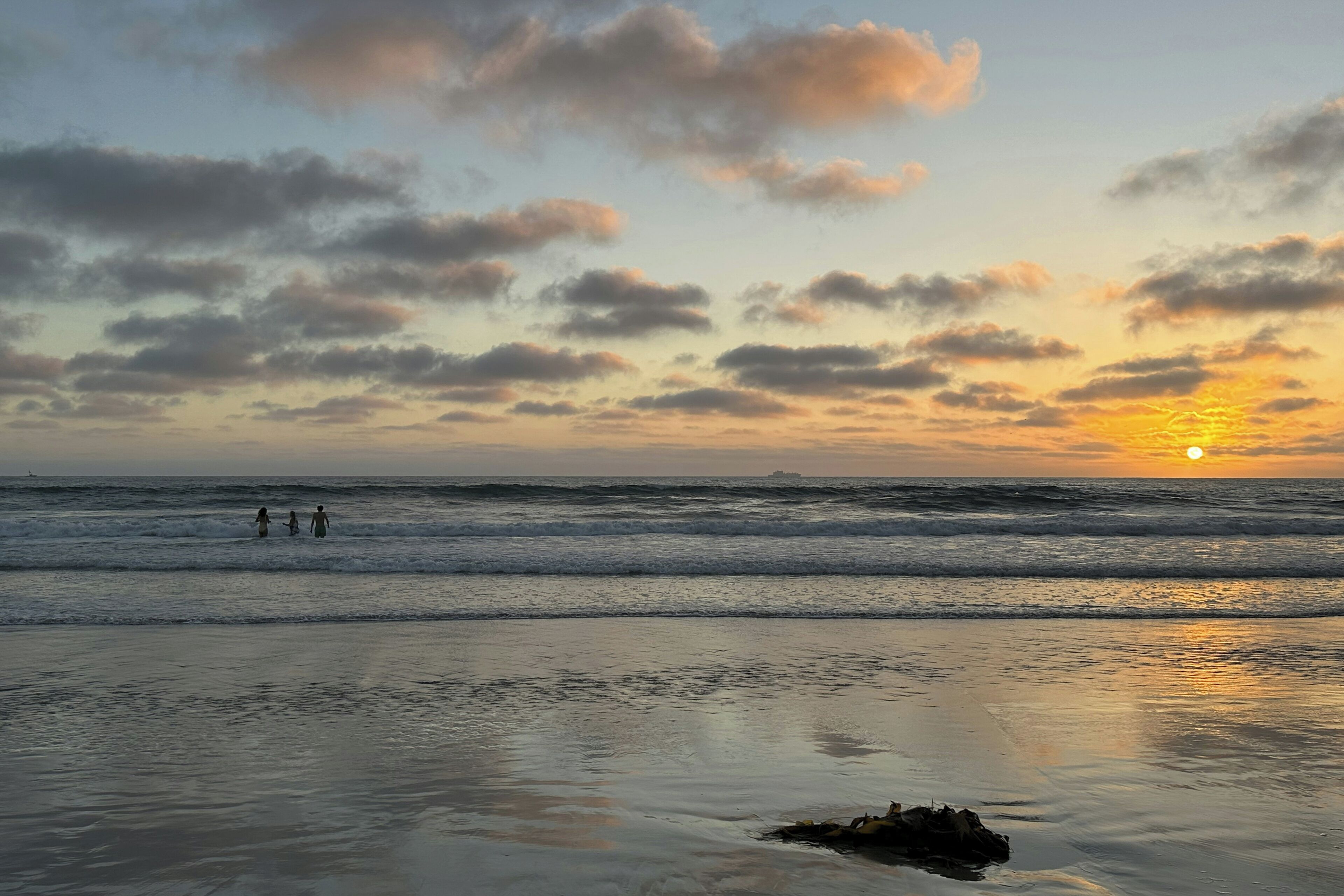 A beach scene with waves, a sunset, and a few people in the distance.