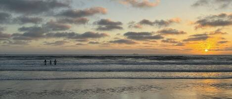 A beach scene with waves, a sunset, and a few people in the distance.