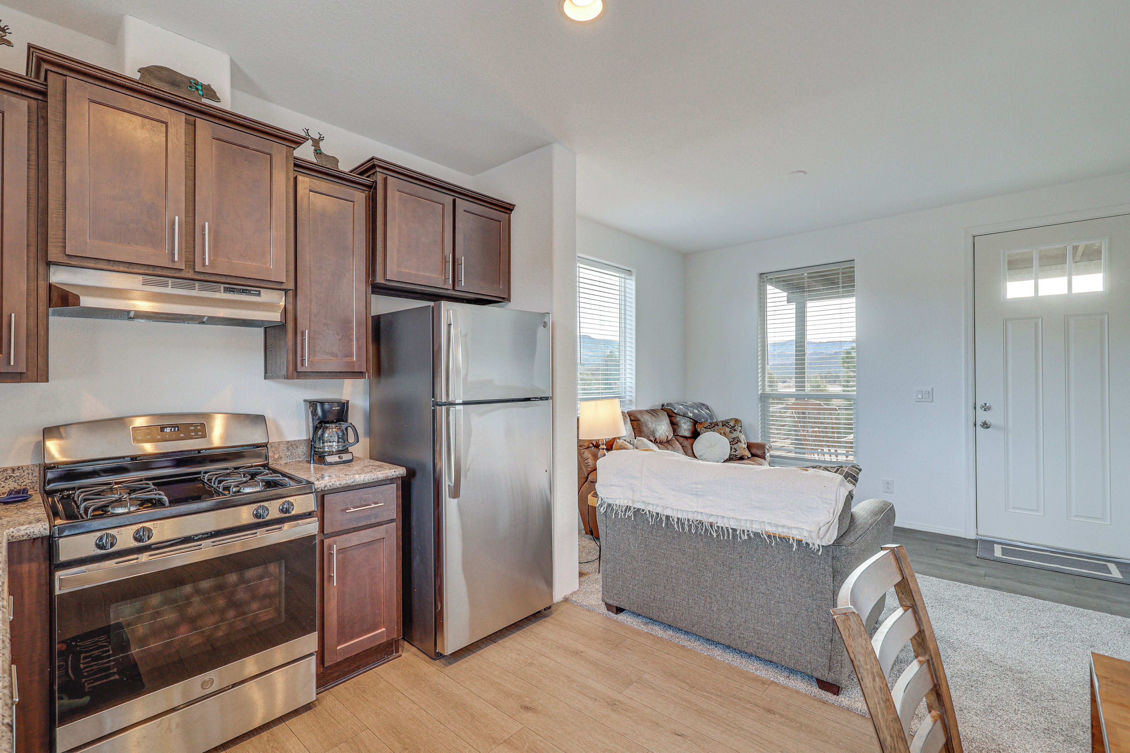 A kitchen with wooden cabinets, stainless steel appliances, and a grey couch in the adjacent living area.
