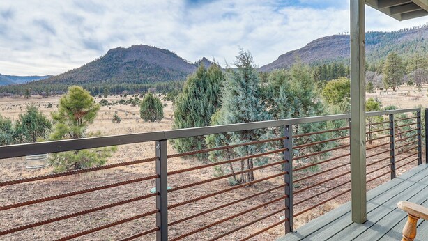 Een balkon met uitzicht op een bergachtig landschap, met een houten terras en metalen hekwerk.