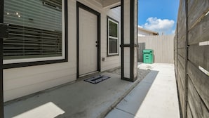 A residential exterior with a white door, a window with blinds, a small porch area, and a green trash bin. - Private Townhouse: Close to Everything (San Antonio)