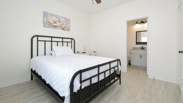 A bedroom with a bed, a ceiling fan, a nightstand, a painting, and a view into the bathroom. - Private Townhouse: Close to Everything (San Antonio)