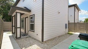 A single-story house with a covered porch, a fenced yard, and a green trash bin. - Private Townhouse: Close to Everything (San Antonio)
