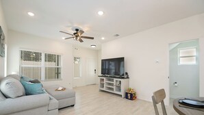 A modern living room with a grey sofa, a TV on a white entertainment unit, a ceiling fan, and a dining area with a table and chairs. - Private Townhouse: Close to Everything (San Antonio)