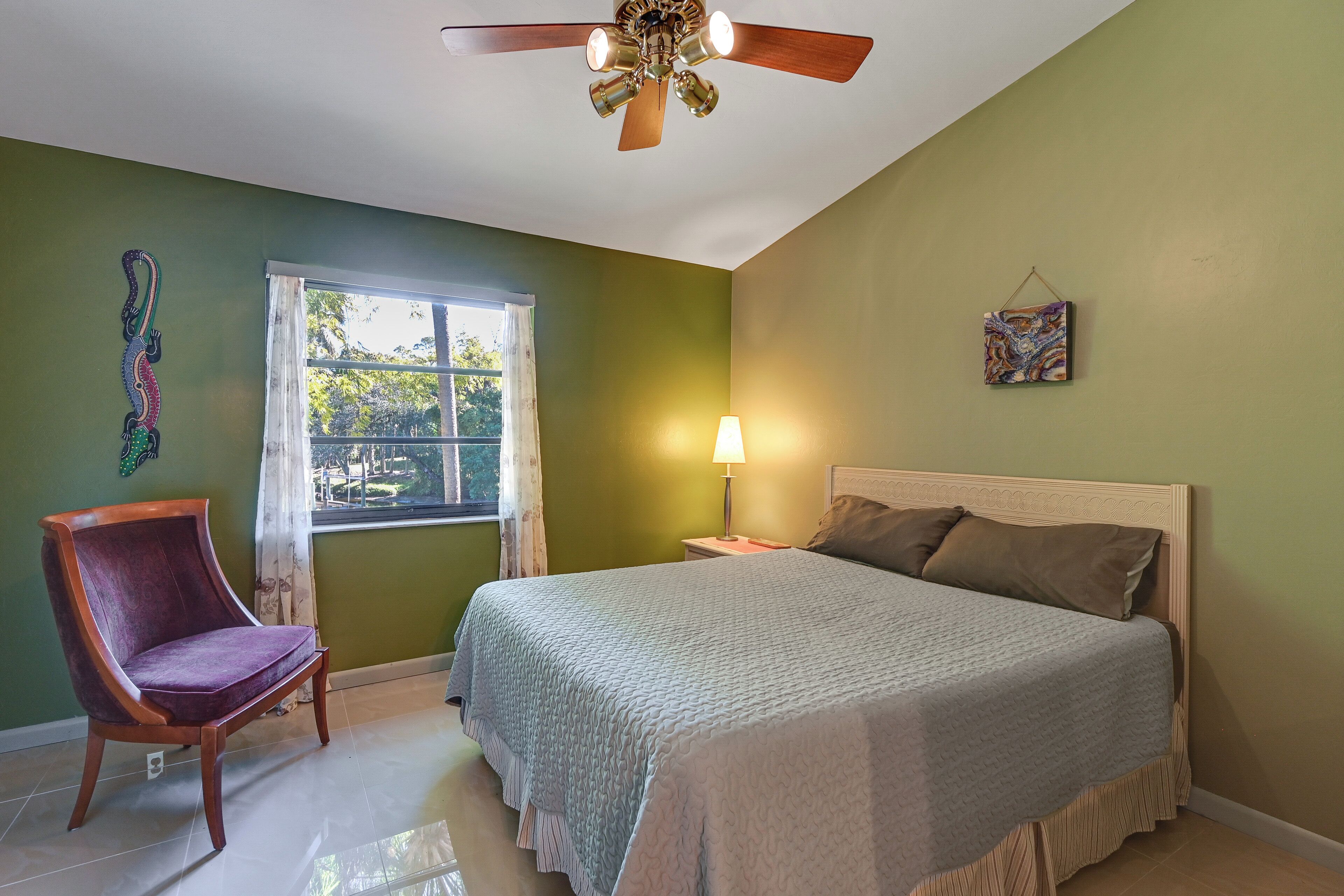 Une chambre à coucher comprenant un lit, une chaise, une fenêtre, un ventilateur de plafond et une lampe fixée au mur.