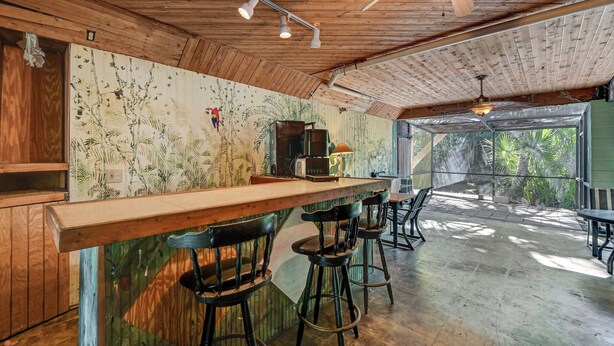 A rustic interior with a wooden bar, bar stools, and a mural of plants on the wall.
