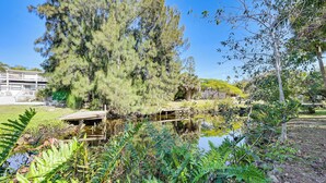 A serene pond with a wooden bridge, surrounded by lush greenery and a large tree.