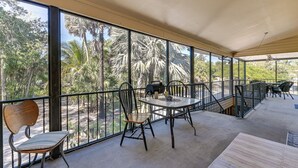 A covered balcony with a table and chairs, a wooden bench, and a view of palm trees.