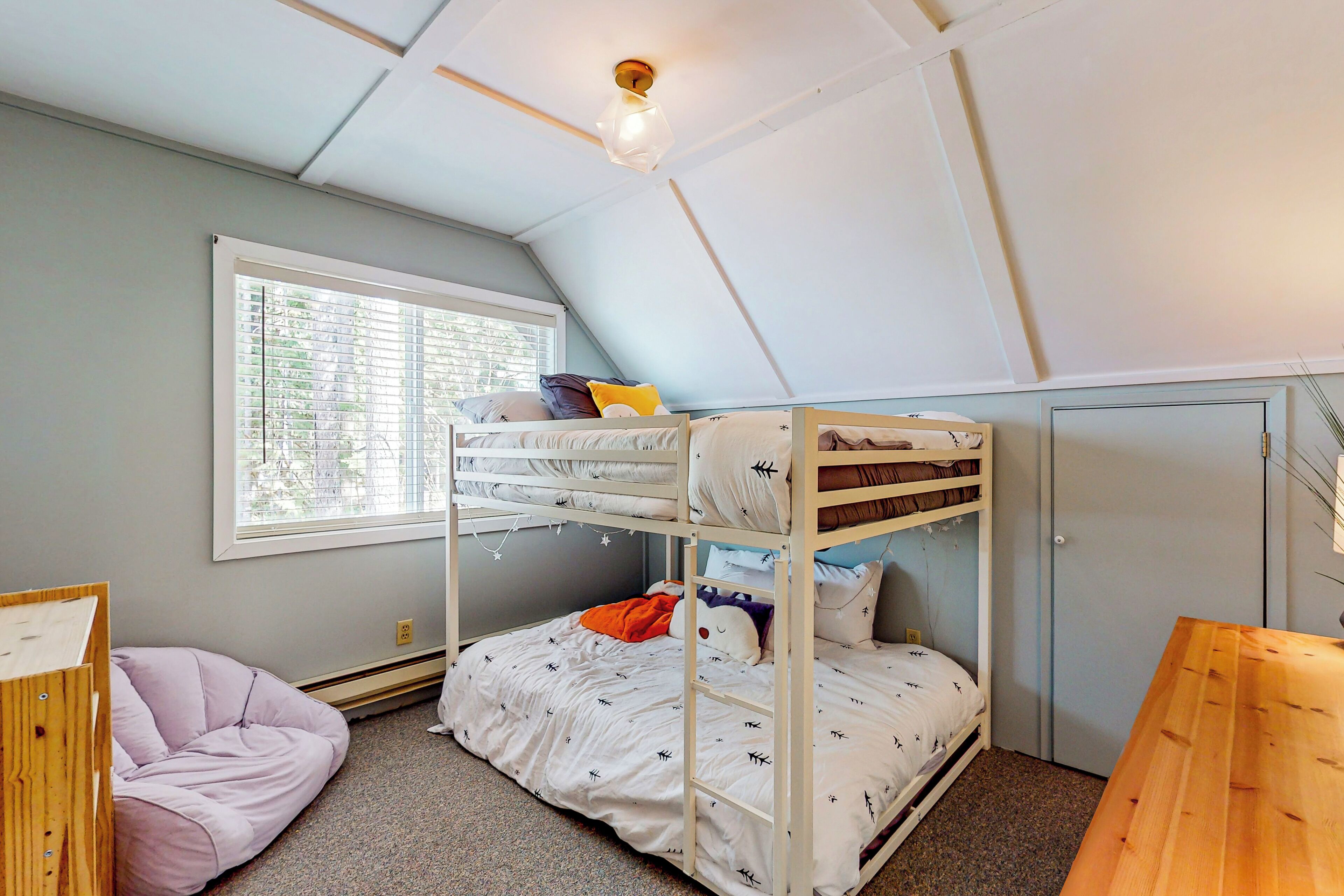 A bunk bed room with a window, a desk, and a bean bag chair.