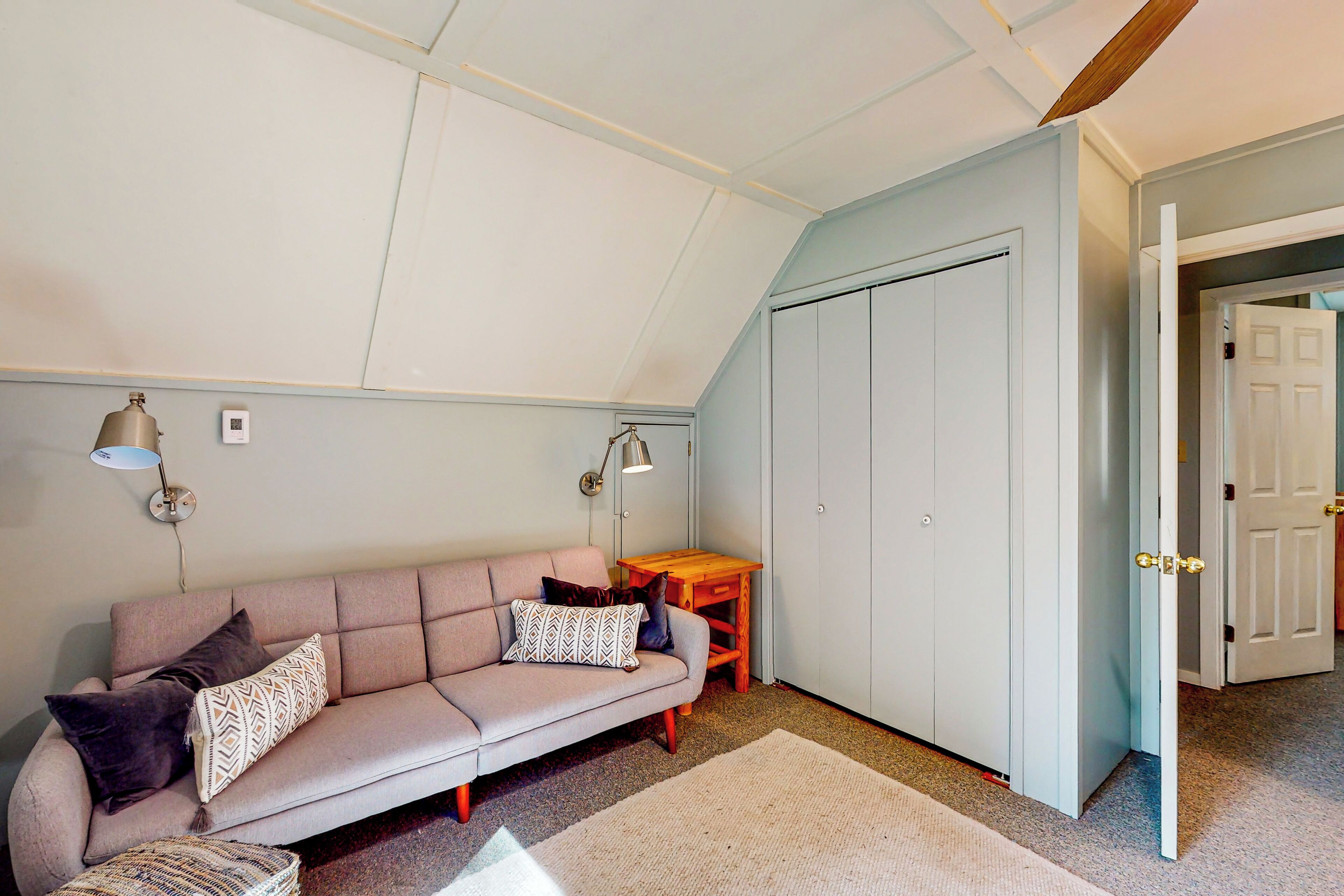 A room with a sofa, a small table, a wardrobe, and a door leading to another room.
