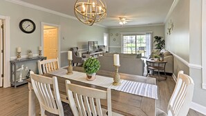 A dining area with a wooden table, white chairs, a chandelier, and a potted plant. - Myrtle Beach Resort Condo Near Golf & Ocean! (Myrtle Beach)