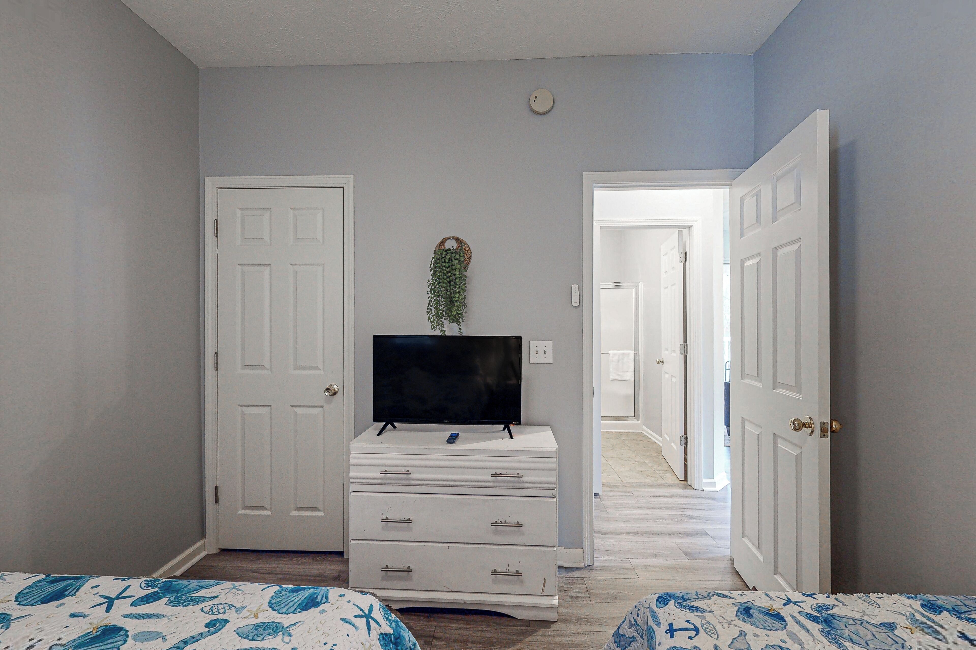 A bedroom with two beds, a dresser, a television, and a hallway leading to another room.