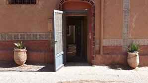 Una entrada con un arcoado de azulejos, una puerta con ornamentación metálica y dos plantas en macetas a cada lado.