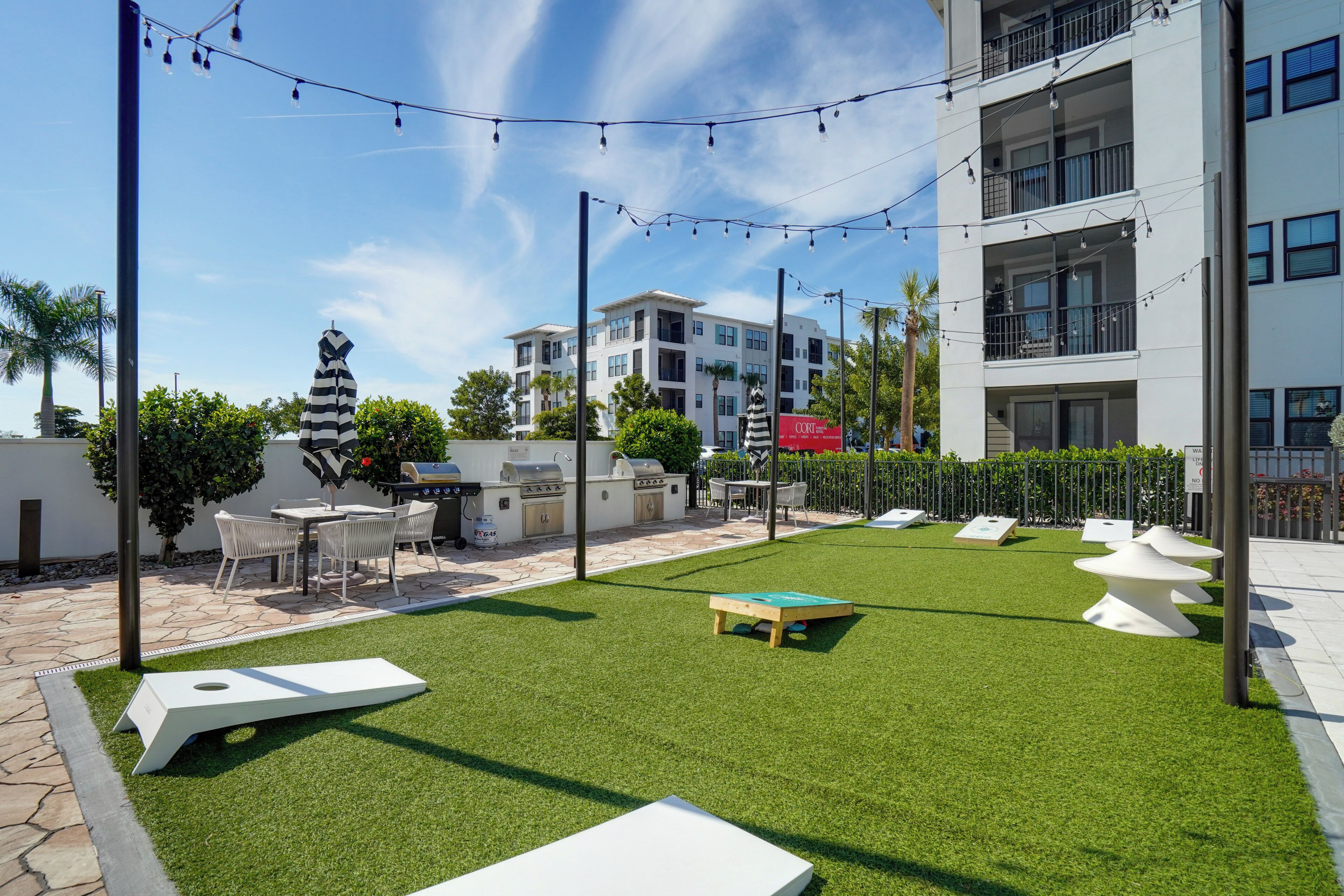 An outdoor patio with artificial grass, white seating, a barbecue area, and string lights.