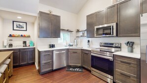 A modern kitchen with stainless steel appliances, dark cabinetry, and a wooden floor. - Beautiful Stucco House in North Hudson (Hudson)