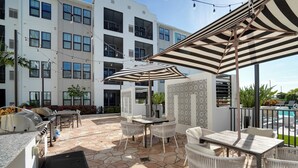 Une terrasse avec un sol en pierre, du mobilier d’extérieur et un espace barbecue.